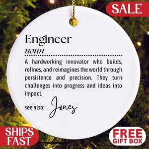 May include: White ceramic ornament with gold hanging string. The ornament features the definition of "Engineer" in black text, including the name "Jones" in cursive. A red "SALE" banner is visible, along with "SHIPS FAST" and "FREE GIFT BOX" labels.