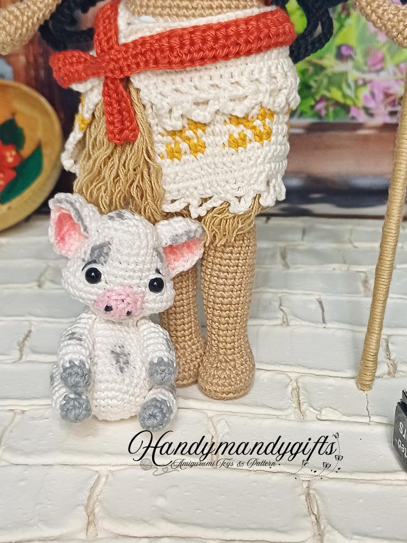 May include: A crocheted doll with a red and white skirt and a small crocheted pig. The doll is standing on a white brick surface. The doll is wearing a red headband and has black hair. The pig is white with black spots and has a pink nose.