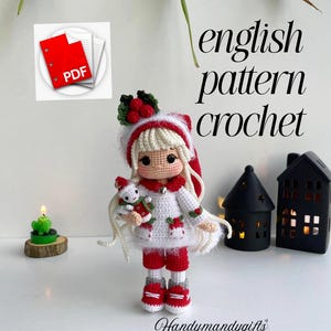 Peut inclure: Poupée au crochet faite à la main, vêtue de rouge et de blanc, tenant un petit animal en peluche. La poupée a de longs cheveux blonds et un chapeau de fête. Le texte "english pattern crochet" et une icône PDF sont inclus.
