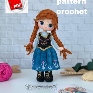 May include: A crocheted doll with auburn plaits, wearing a blue dress with white floral embroidery and a black bodice. The doll has blue eyes and is labeled "english pattern crochet". A PDF icon is in the upper left.