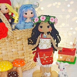Peut inclure: Poup&eacute;e en crochet avec des cheveux bruns, une couronne de fleurs et une robe rouge et blanche. La poup&eacute;e est debout sur une base en bois et tient un petit agneau en crochet. La poup&eacute;e est entour&eacute;e d'autres poup&eacute;es et jouets en crochet, dont un champignon et un panier.