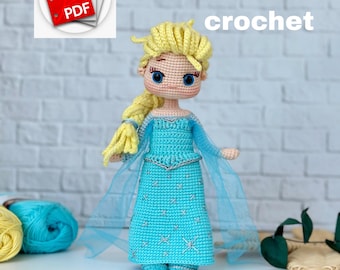 Op de afbeelding: Een handgemaakte gehaakte pop in een lichtblauwe jurk met een sterrenpatroon, blond haar en blauwe ogen. De pop heeft een lange vlecht en draagt een doorschijnende blauwe cape. De afbeelding bevat de tekst "english pattern crochet".