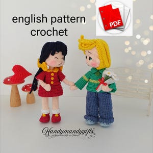 Pode incluir: Bonecas de crochê, uma menina com um vestido vermelho e um menino com um suéter verde e calças azuis, de mãos dadas. O menino segura um buquê de flores brancas. As palavras "english pattern crochet" estão no topo. Um ícone PDF está no canto superior direito.