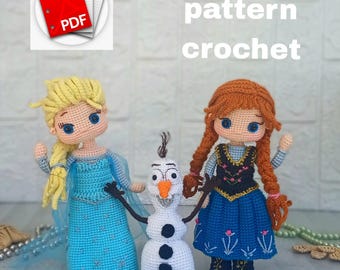 Op de afbeelding: Gehaakte poppen van Elsa, Anna en Olaf uit de film Frozen. Elsa draagt een blauwe jurk met een cape, Anna heeft een zwart lijfje en een blauwe rok, en Olaf is een witte sneeuwman. De woorden "english pattern crochet" zijn zichtbaar.
