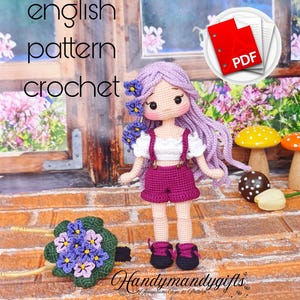 Op de afbeelding: Een handgemaakte gehaakte pop met paars haar en een bijpassende outfit, inclusief een korte broek en bretels. De pop is versierd met bloemen en wordt vergezeld door een gehaakt boeket. De tekst "english pattern crochet" en een PDF-pictogram zijn ook aanwezig.