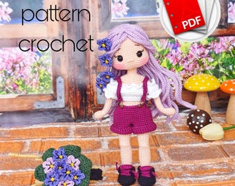 May include: A handmade crochet doll with purple hair and a matching outfit, including shorts and suspenders. The doll is adorned with flowers and is accompanied by a crochet bouquet. The image also includes the text "english pattern crochet" and a PDF icon.