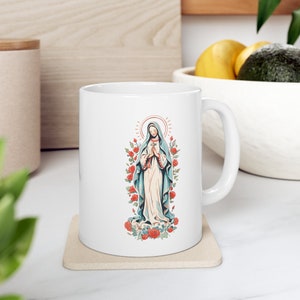 May include: White ceramic mug featuring a colourful illustration of the Virgin Mary surrounded by red roses. The illustration is in a vintage style.