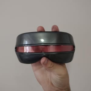 May include: A black and red visor with a reflective surface. The visor is made of plastic and has a curved shape.