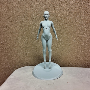 May include: A light gray, stylized human figure, standing on a circular base. The figure has a smooth, minimalist design, with articulated joints and a neutral expression. The figure is approximately 12 inches tall.