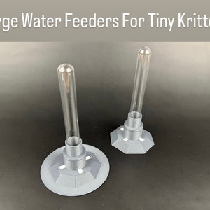 May include: Two clear glass water feeders with grey plastic bases. The bases have a hexagonal shape with small holes for ventilation.  Large Water Feeders For Tiny Critters.