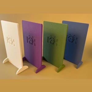 Op de afbeelding: Vier kleurrijke, vrijstaande panelen in wit, paars, groen en blauw. Elk paneel heeft een rechthoekige vorm met een voet voor stabiliteit en een verdiept logo. De panelen zijn in een rij gerangschikt tegen een neutrale achtergrond.