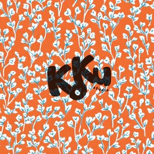 May include: Orange fabric with a repeating pattern of white and blue floral branches. The text "Kku studio" is in the lower right corner, in a dark brown color.