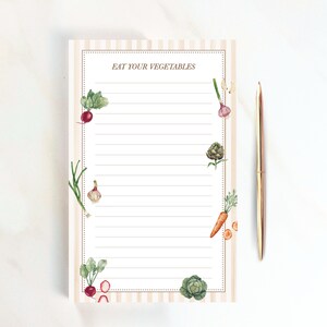 May include: A rectangular notepad with light beige vertical stripes and a dotted border, featuring the text EAT YOUR VEGETABLES at the top. The page is lined and decorated with watercolor illustrations of radishes, garlic, artichokes, and carrots.