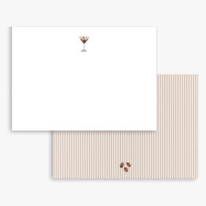 May include: Two-piece stationery set featuring a white notepad with a cocktail illustration and a striped backing sheet. The cocktail is a brown martini with a garnish. Three coffee beans are on the striped sheet.