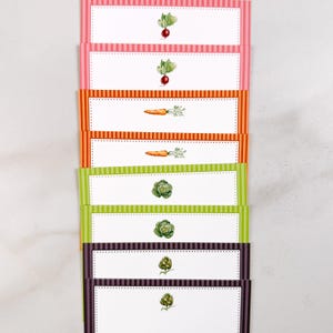 May include: A set of eight rectangular paper labels arranged in a vertical stack. Each label features a white center with a dotted border, surrounded by a striped frame in pink, orange, lime green, or dark purple, each with a vegetable illustration.