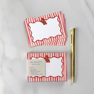 May include: A set of 30 mini cards with a red and white striped design, scalloped edges, and a berry cluster accent. The cards are in a clear box with a gold pen.