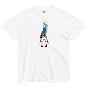 Pode incluir: Camiseta branca com um gráfico de uma formiga de desenho animado azul fazendo um enterramento sobre um jogador de basquete vermelho e branco.