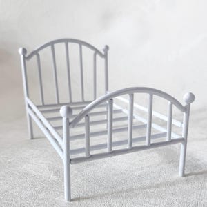 Peut inclure: Un petit cadre de lit en métal blanc avec une tête de lit et un pied de lit incurvés. Le lit a une base à lattes et quatre pieds. Le cadre est peint en blanc mat uni. Le lit est conçu pour les poupées ou autres petites figurines.