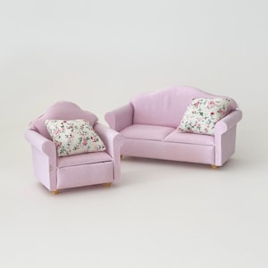 May include: Miniature pink sofa and armchair set. Each piece has a floral patterned pillow. The furniture is made of a soft, textured material and has small wooden legs. Perfect for a dollhouse or miniature scene.