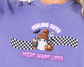 Könnte beinhalten: Lilafarbenes T-Shirt mit kurzen Ärmeln und einem Aufdruck eines Geisters, der eine Mütze trägt und einen Kürbis und eine Kaffeetasse hält. Der Text "Feeling Cute Might Haunt Later" ist auf dem Shirt gedruckt.