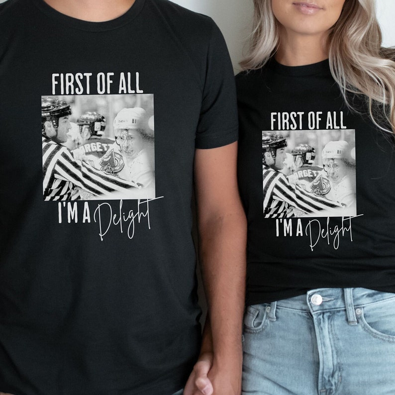 Może przedstawiać: Dwie czarne koszulki z białym nadrukiem graficznym. Grafika przedstawia czarno-białe zdjęcie dw&oacute;ch hokeist&oacute;w z tekstem "First of all, I'm a Delight".