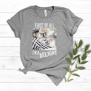 Pu&ograve; includere: Maglietta grigia con il testo "First of all I'm a delight" e una foto di un giocatore di hockey che riceve una penalit&agrave;.