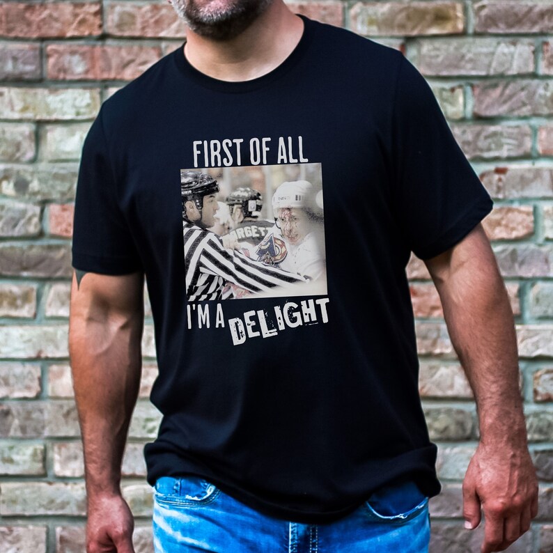 Man wearing a black t-shirt with a graphic of an angry hockey player. The shirt reads First of All Im a Delight