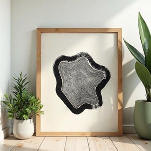 Könnte beinhalten: Ein gerahmter Kunstdruck mit einer schwarzen Baumring-Querschnittsgrafik, die auf einem cremefarbenen Hintergrund zentriert ist. Das Kunstwerk befindet sich in einem hellen Holzrahmen und zeigt detaillierte, konzentrische Jahresringe.
