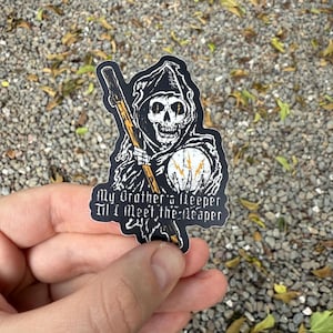 May include: A black sticker featuring a Grim Reaper design with a skull, holding a scythe. The sticker includes the text "My Brother's Keeper Til I Meet the Reaper" in a gothic font. The Reaper is depicted with a hooded cloak and a glowing orb.