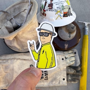May include: A sticker of a cartoon character wearing a yellow jacket and a hard hat. The character is giving a rock and roll hand gesture. The sticker is on a white background and has the text "Hard Money Marts" on the bottom right corner.