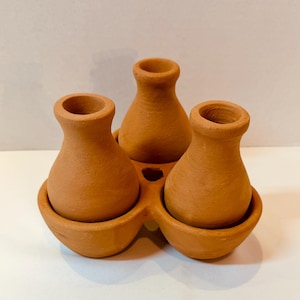 May include: A terracotta ceramic planter with three small vases. The vases are connected by a base with three rounded compartments. The color is a warm, earthy brown. The planter is designed to hold small plants or flowers.