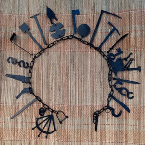 Może przedstawiać: Czarny metalowy łańcuch z różnymi narzędziami i kształtami przymocowanymi. Łańcuch jest w kształcie koła, a narzędzia skierowane są na zewnątrz. Narzędzia obejmują piłę, nóż, klucz, młotek, śrubokręt, szczypce, hak, klucz, otwieracz do butelek, kompas i podkowę.