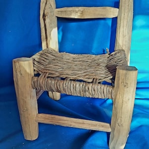May include: A small wooden stool with a woven straw seat. The stool is made of rough-hewn wood and has a rustic appearance.
