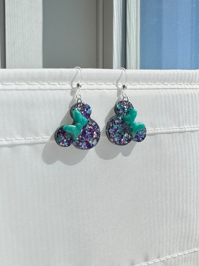 May include: A pair of silver dangle earrings with black and green glitter resin Mickey Mouse heads.
