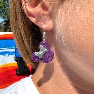 May include: Purple glitter earrings shaped like Mickey Mouse heads with silver glitter accents. For scale only.