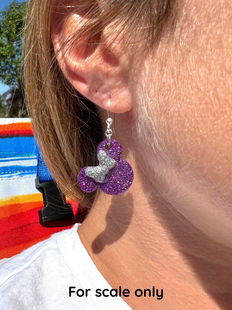 May include: Purple glitter earrings shaped like Mickey Mouse heads with silver glitter accents. For scale only.