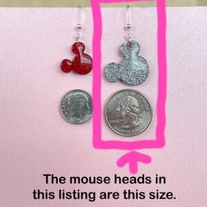 May include: A pair of silver dangle earrings with red and silver glitter mouse head charms. The mouse heads are approximately the size of a US quarter.