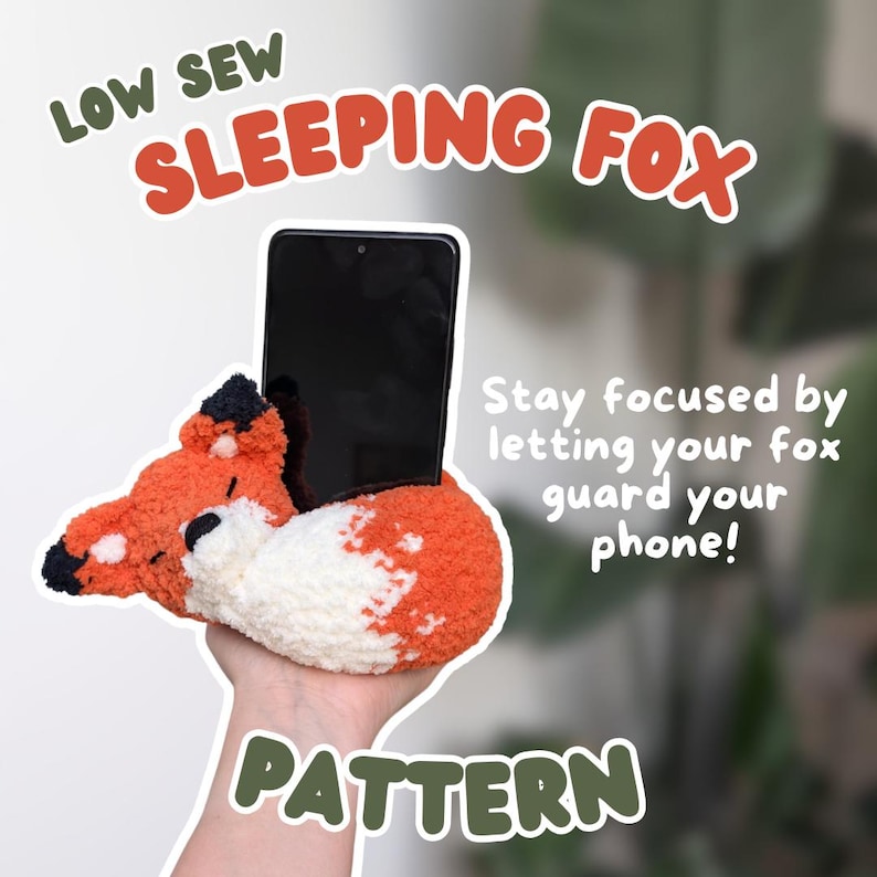 Puede incluir: Un soporte para tel&eacute;fono con forma de zorro naranja y blanco con un tel&eacute;fono inteligente negro. El texto de la imagen dice "LOW SEW SLEEPING FOX PATTERN". El zorro sostiene el tel&eacute;fono. El texto tambi&eacute;n dice "&iexcl;Mantente concentrado dejando que tu zorro proteja tu tel&eacute;fono!"