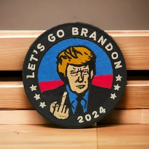 Puede incluir: Un parche bordado en blanco y negro con un retrato de un hombre con cabello rubio. El parche tiene el texto "Let's Go Brandon 2024" alrededor del borde.