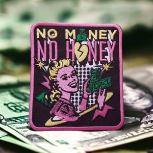 Könnte beinhalten: Gestickter Aufnäher mit rosa Rand und dem Text "NO MONEY NO HONEY". Der Aufnäher zeigt eine Retro-Illustration einer Frau, die Geld, ein gebrochenes Herz und einen Geldsack hält.