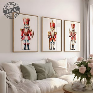 May include: Three watercolor paintings of nutcracker soldiers in red and gold uniforms, each with a different pose and expression. The paintings are framed in gold and hung on a white wall.