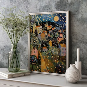 May include: A framed art print depicting a whimsical village scene under a starry night sky. The artwork features colorful houses, trees, and a winding path, with a large moon and stars. The print is displayed on a white surface with a vase of greenery and a candle.