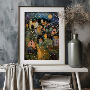 May include: A framed art print depicting a whimsical village scene under a starry night sky. The artwork features colorful houses, trees, and a winding path, all rendered in a painterly style. The frame is gold-toned, and the print is displayed on a white shelf.