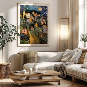 May include: A framed painting of a whimsical village scene with colorful houses, trees, and a winding path. The sky is filled with stars and a crescent moon. The painting is set against a white wall in a living room setting.