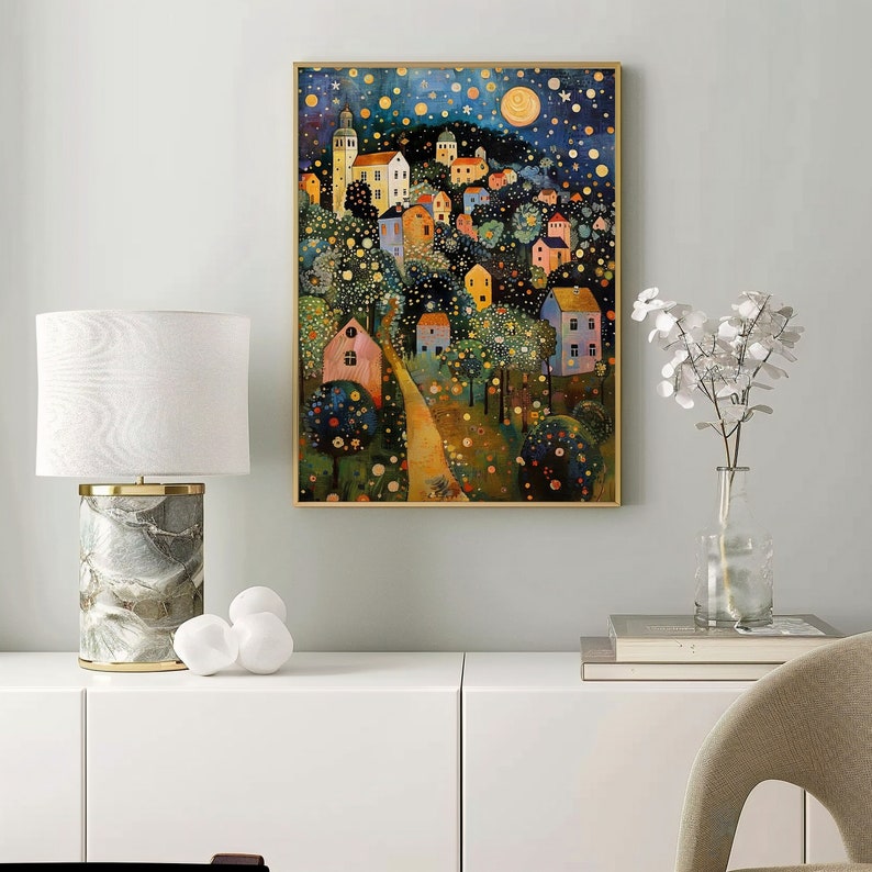 May include: A framed art print depicting a whimsical village scene under a starry night sky. The artwork features colorful houses, trees, and a winding path, with a gold-colored frame. The overall theme is a dreamy, artistic landscape.