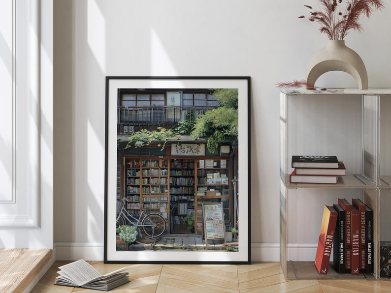 May include: A framed photograph of a bookstore in Japan. The storefront is lined with bookshelves filled with books. A bicycle is parked in front of the store. The store is decorated with plants and flowers.