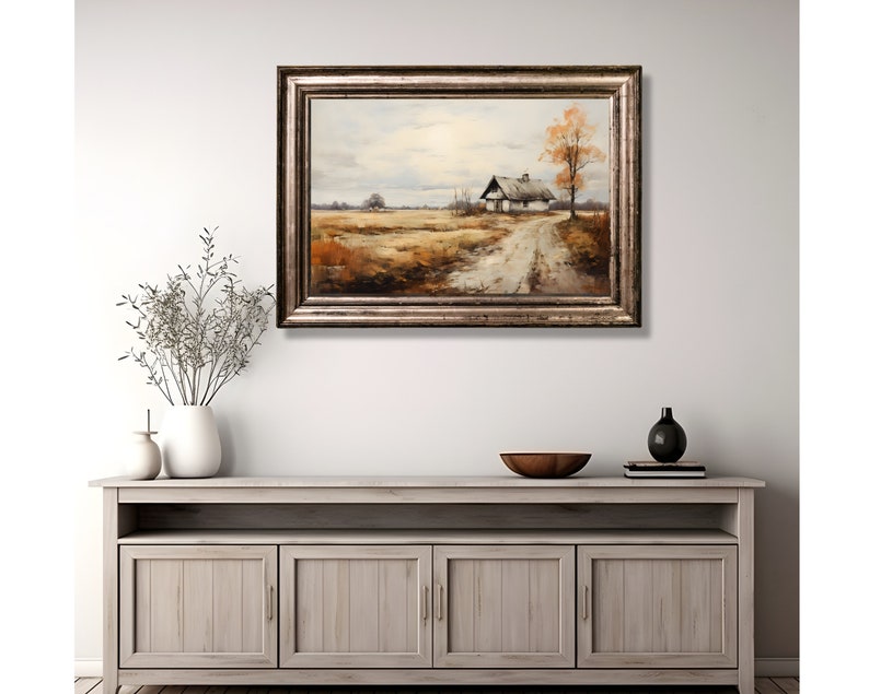May include: A framed oil painting depicting a rural landscape with a small white house and a dirt road leading to it. The house is surrounded by trees and fields, and the sky is cloudy. The painting is framed in a silver frame.