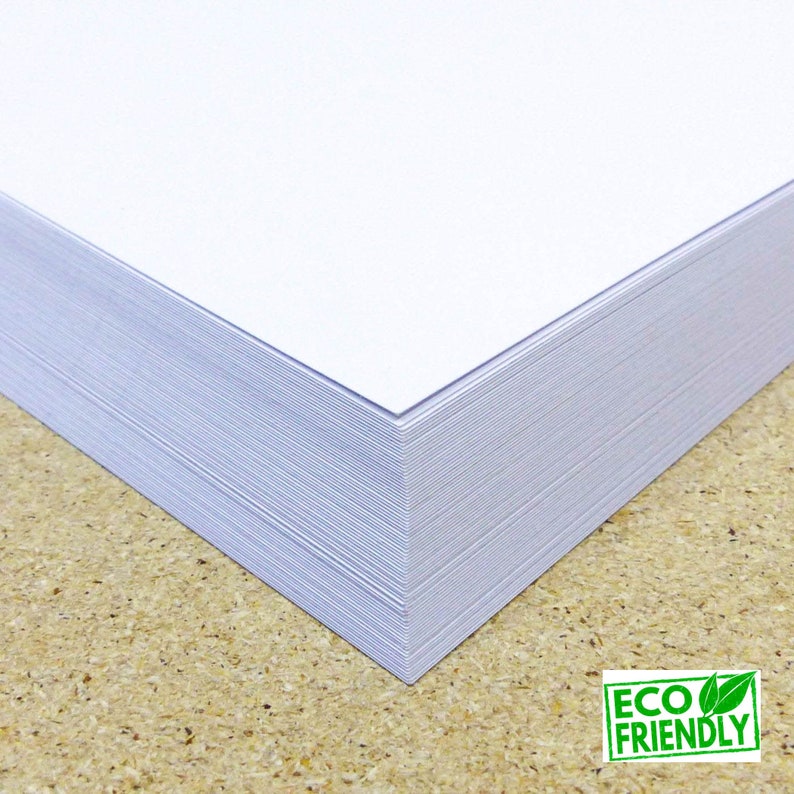 May include: A stack of white paper, likely printer paper, with a corner folded over. The paper is on a brown surface. The text "ECO FRIENDLY" is visible in green letters on a green leaf background.