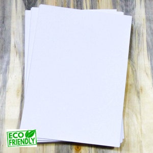 May include: A stack of white paper sheets on a wooden surface. The paper is eco-friendly.