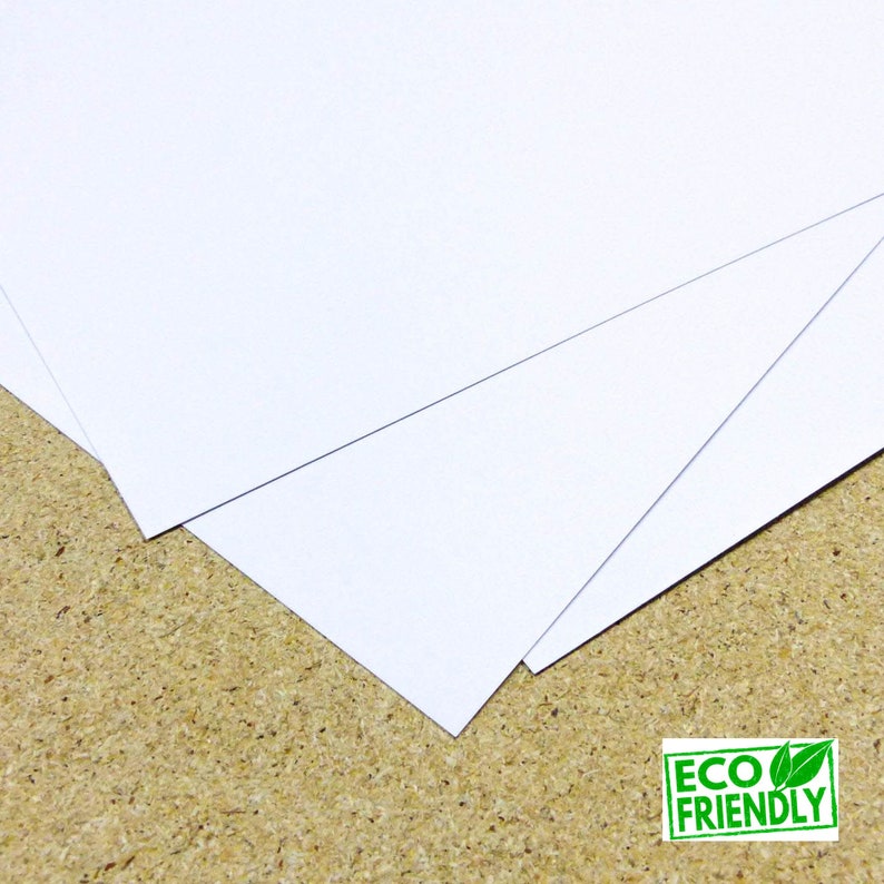 May include: Stack of white cardstock paper, eco-friendly, on a brown surface.